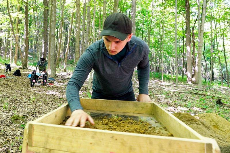 A+college+student+works+at+an+archaeology+dig+in+the+woods