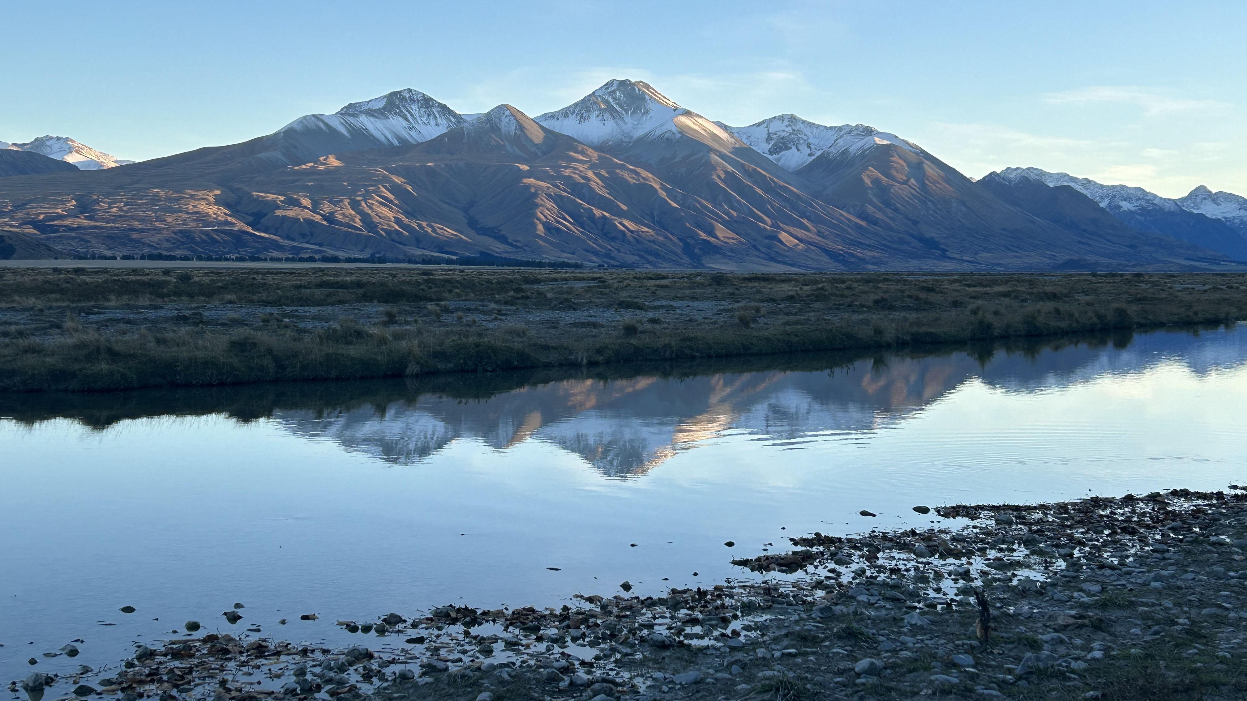 A gorgeous view of a stretch of mountains in New Zealand, reflecting in a stream.